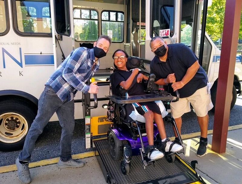 Two transportation employees on either side of a smiling adult on a wheel chair lift