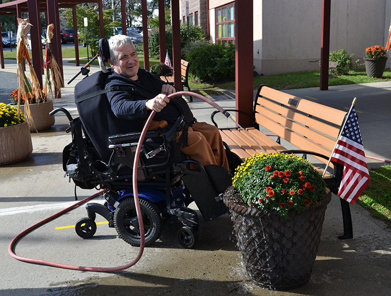 Man in a wheel chair watering plants with a hose