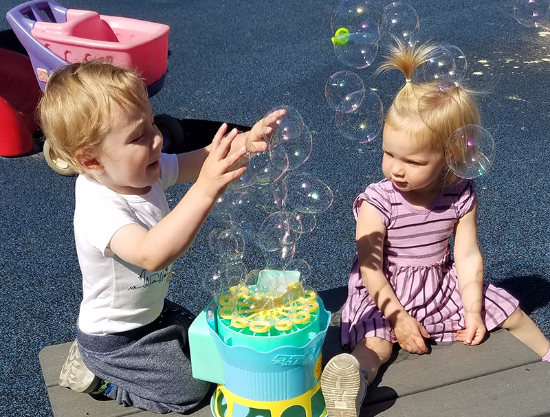 Two children enjoying a bubble blowing machine