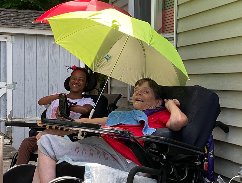 Two women in wheel chairs enjoying outdoor activity with an umbrella
