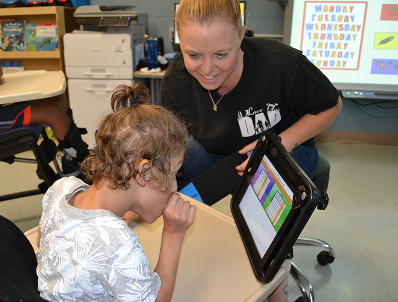 Teacher showing boy to use assistive technology device